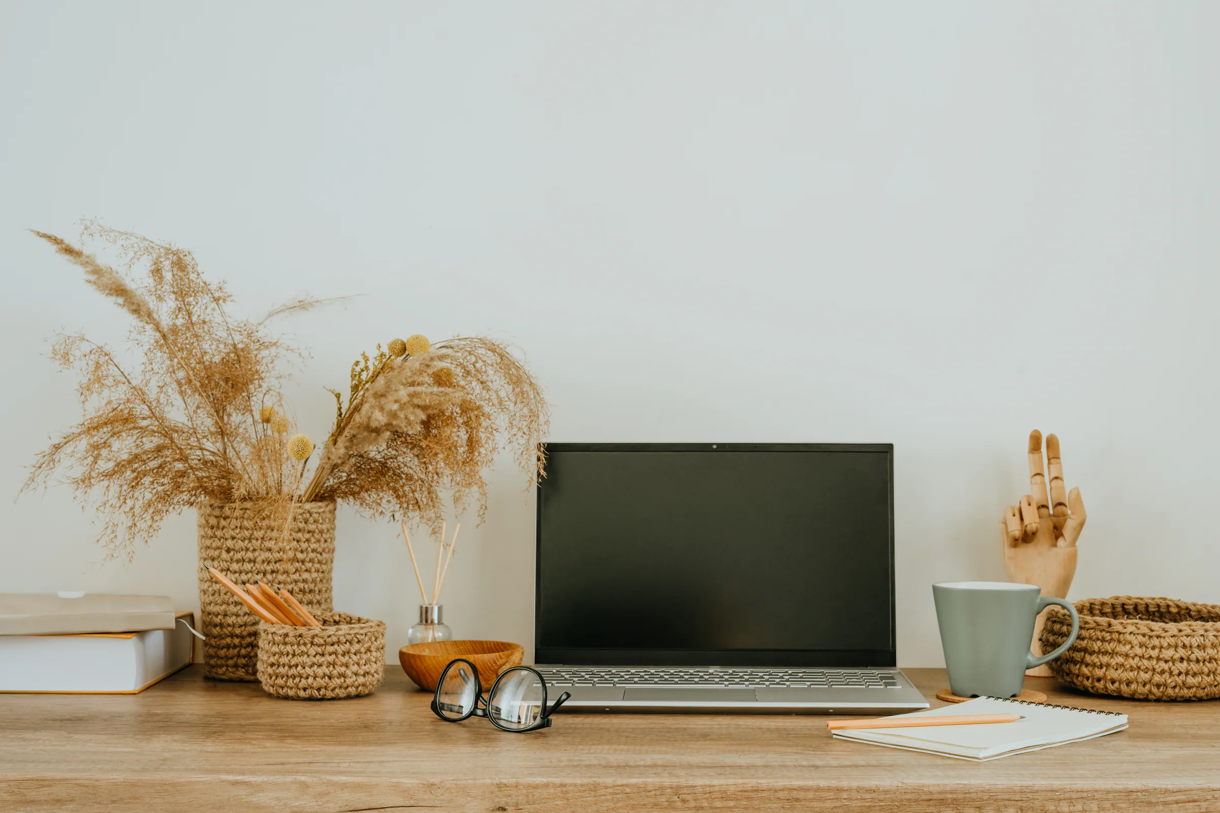 A wooden desk with a laptop, dried grasses and a cup