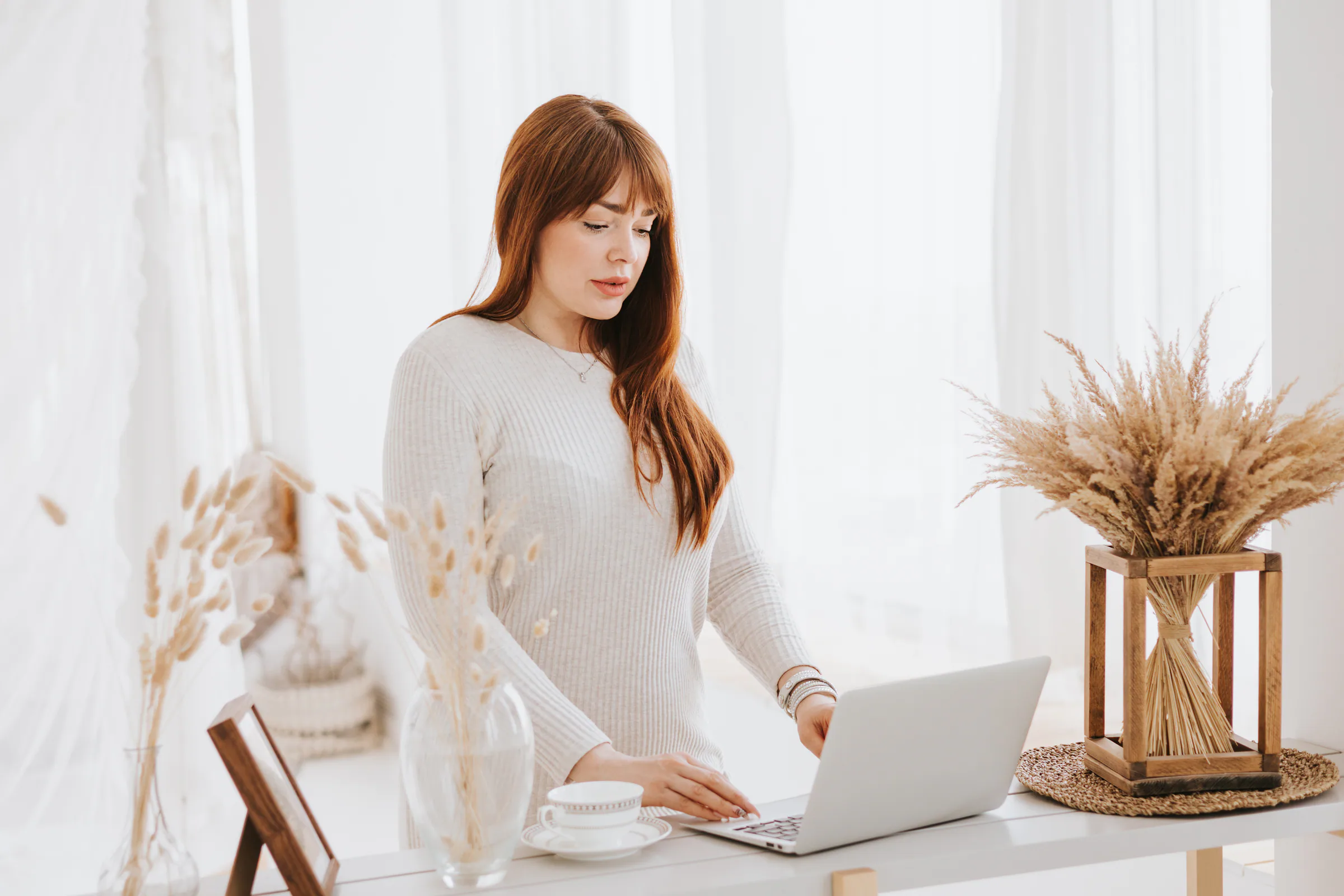 A woman working on a laptop in a bright office with dried grasses